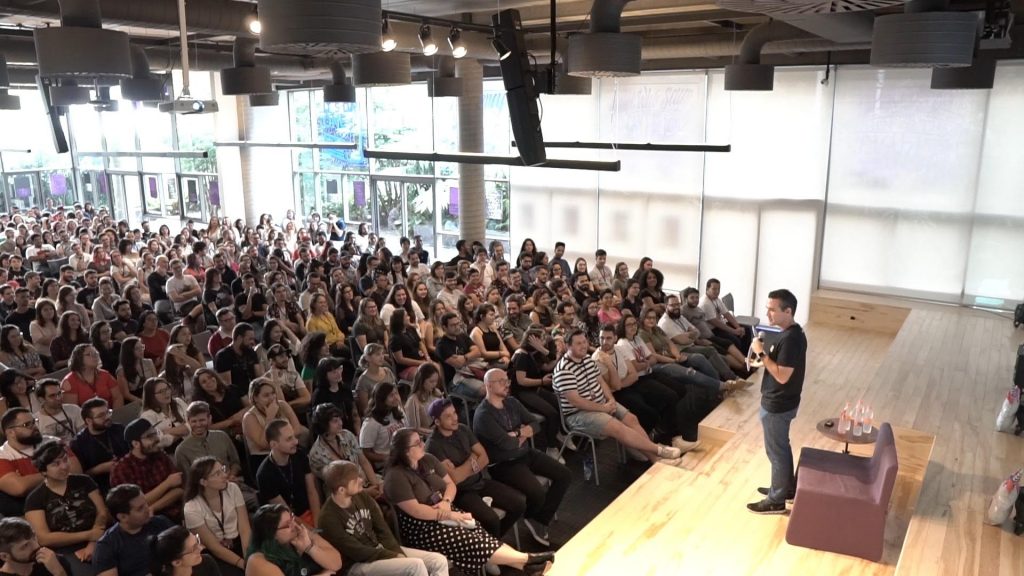 O auditório do Nubank, com mais de 300 pessoas sentadas, e o CEO David Velez falando no palco