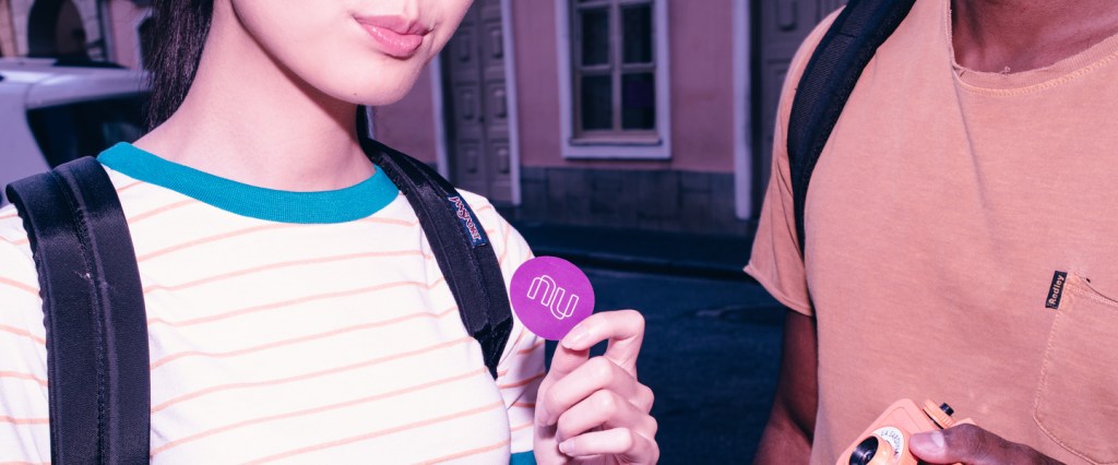 NuConta: Mulher de blusa listrada segurando adesivo do Nubank.