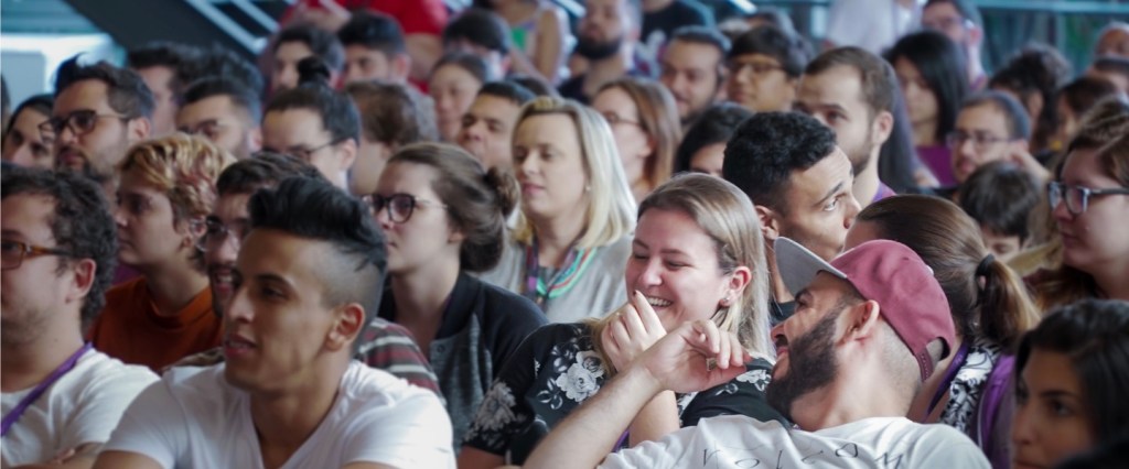 Grupo de pessoas sentadas em um auditório sorrindo