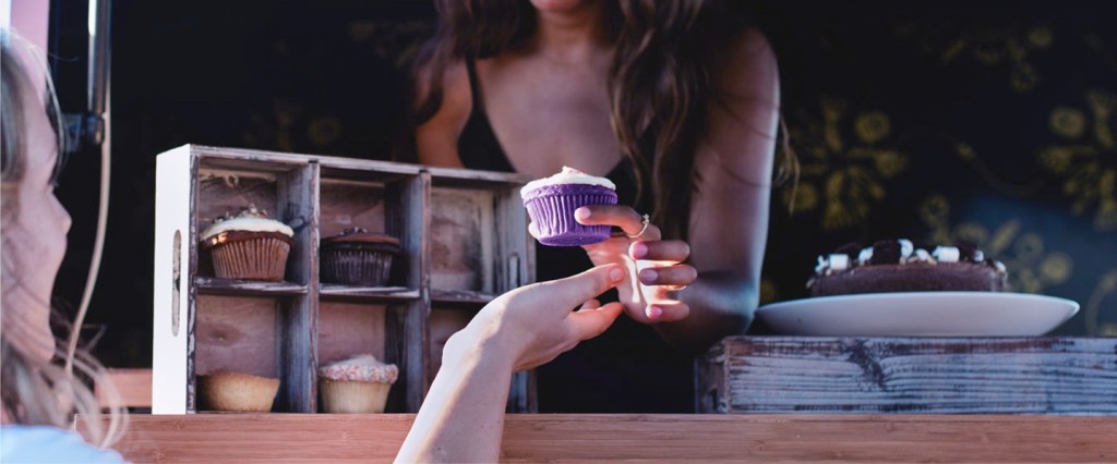 Lista de espera conta PJ nubank: imagem mostra uma jovem vendendo um cupcake roxo e uma mão estendida para pegar o produto