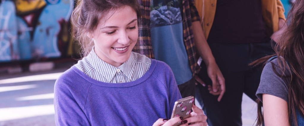 Renomear compras pelo app: uma garota sentada usando suéter roxo usando um celular