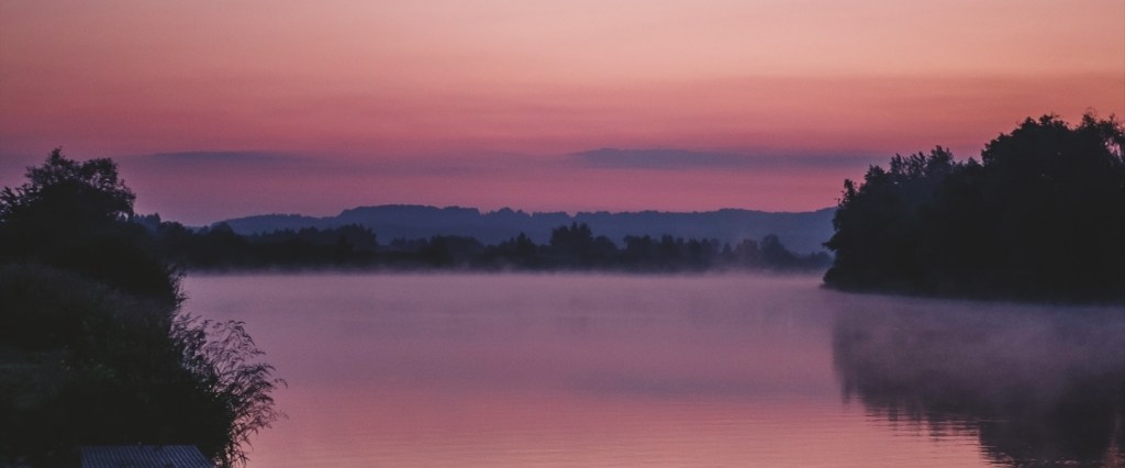 Abri a NuConta porque rende mais que a poupança: imagem em tons de roxo de um lago e árvores.