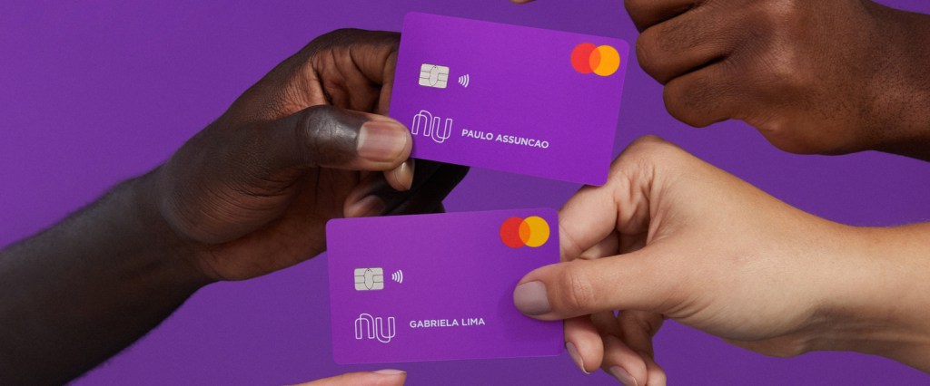 Mãos segurando cartões Nubank em um fundo roxo