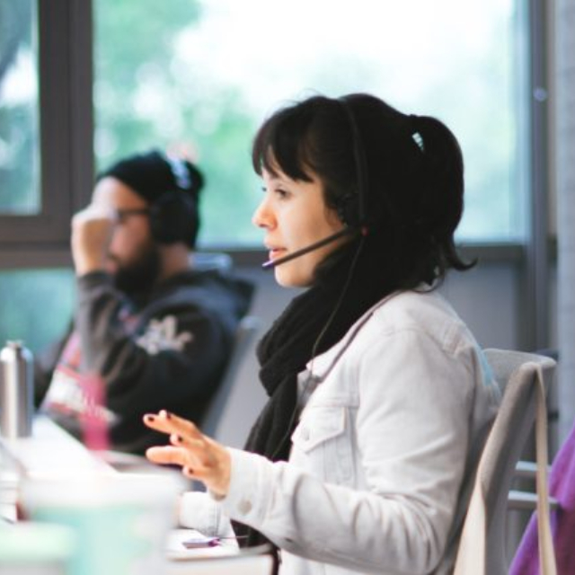 Atendimento Nubank: Três pessoas trabalhando no escritório do Nubank. O foco da foto está em uma mulher, jovem, atendendo clientes com um headphone