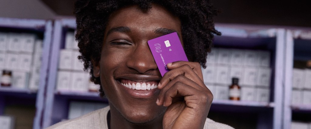 Mastercard Surpreenda: homem sorrindo segurando um cartão de crédito Nubank na frente do rosto