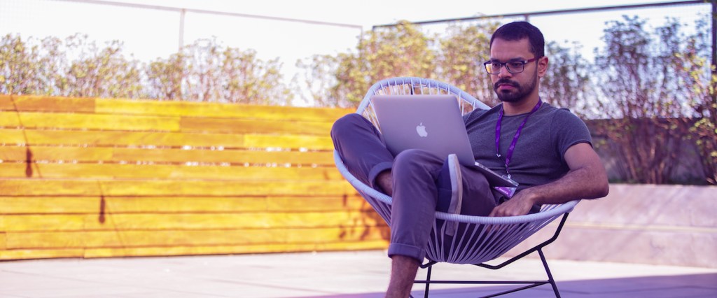 Onboarding remoto Nubank: homem sentado em uma cadeira num terraço com o computador no colo.