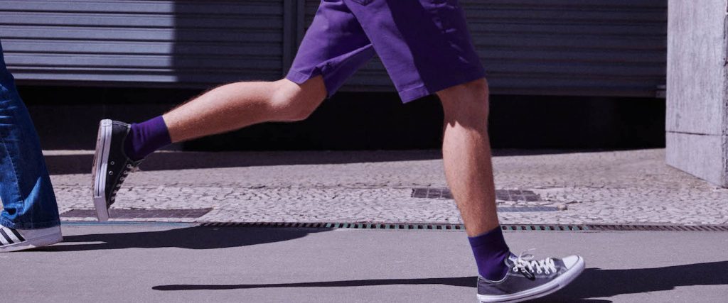 Nubank Status Quo: um homem (da cintura pra baixo) correndo com meias e bermuda roxas, camiseta branca e mochila nas costas.