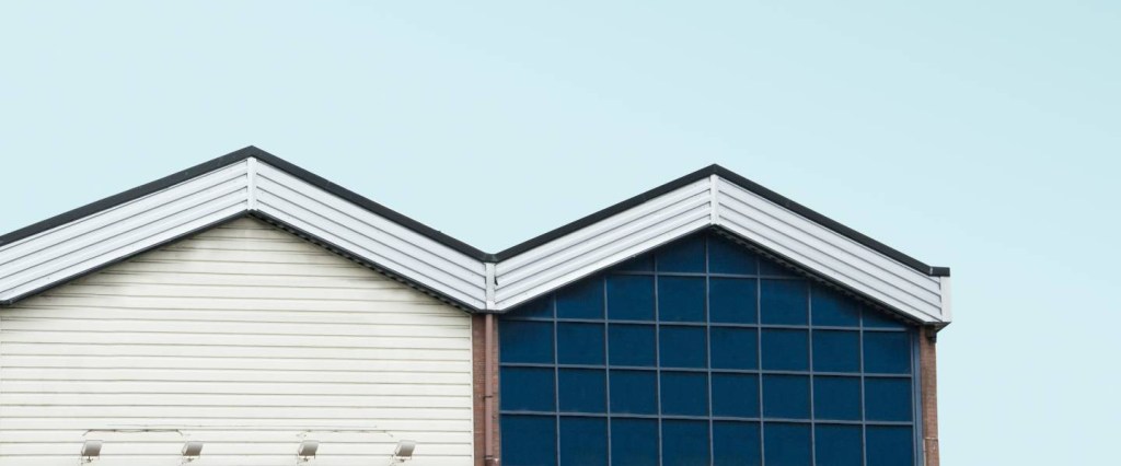 Imagem mostra o teto de uma casa, com uma parede azul e branca, e um céu azul ao fundo.