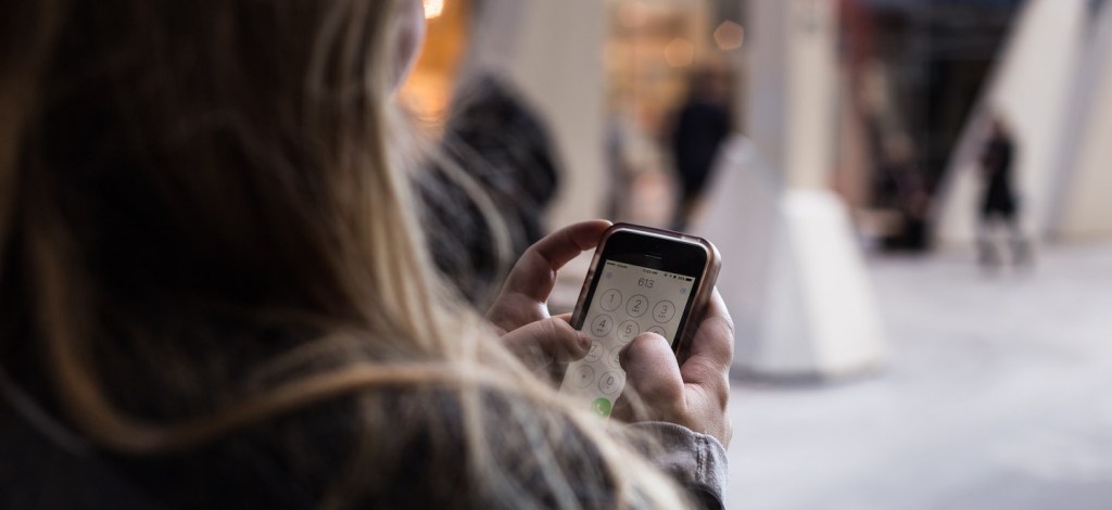 Uma mulher de costas com um celular em mãos, colocando a senha de desbloqueio da tela. Foto: Priscilla Du Preez