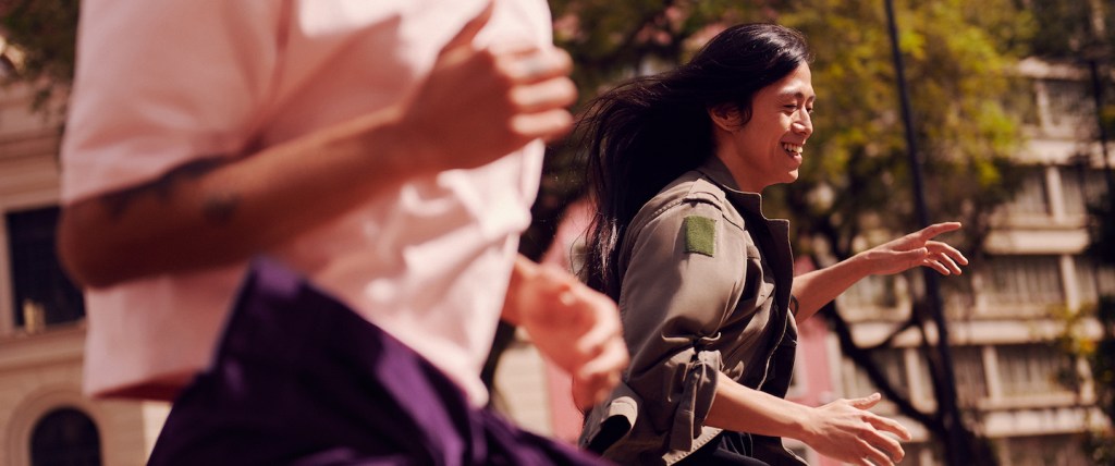 Pessoas correndo ao ar livre. Uma das pessoas está em evidência na foto, é uma mulher sorrindo