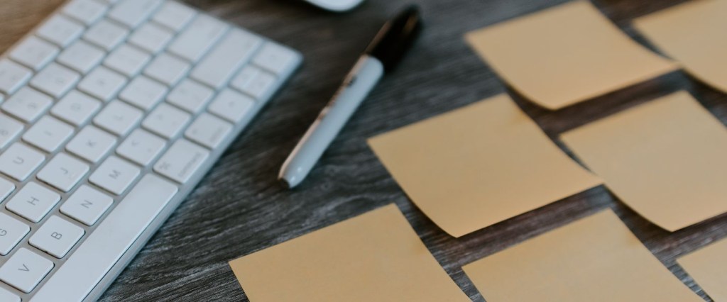 Prestação de serviços: imagem de um teclado com uma caneta ao lado e post its amarelos. Foto: @kellysikkema/ Unsplash