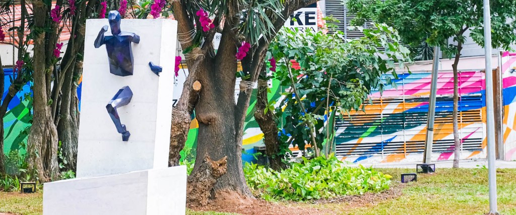 Imagem de uma estatua em uma praça. A estatua é uma figura rompendo uma barreira