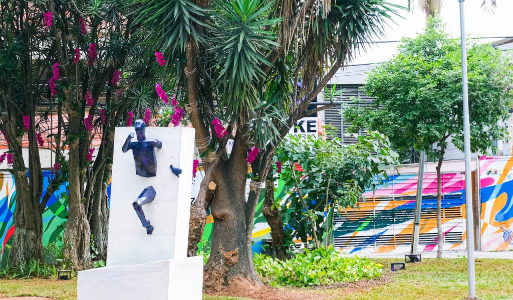 Imagem de uma estatua em uma praça. A estatua é uma figura rompendo uma barreira