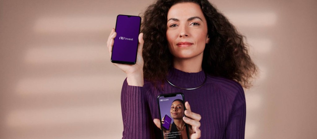 Mulher branca vestindo uma blusa roxa segura dois celulares, um em cada mão, onde é possível ver o logotipo da NuInvest - Informe de rendimentos da NuInvest