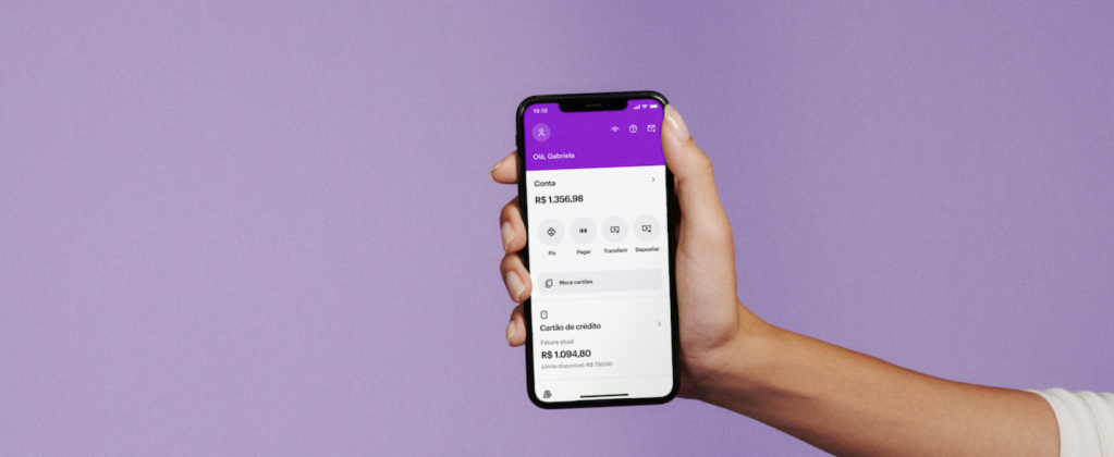 Uma mão segurando um celular mostrando a nova tela inicial do app do Nubank.