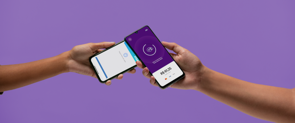 Na imagem, é possível visualizar um pagamento sendo feito com o NuTap. Uma mão segura um celular onde aparece a tela de cobrança do app. Outra, segura outro celular com carteira virtual, fazendo um pagamento por aproximação.