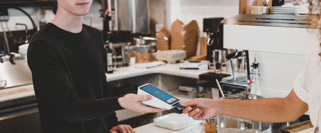 maquininha de cartão: imagem de uma compra por maquininha de cartão em um ambiente que parece um café. Foto: @ClayBanks Unsplash