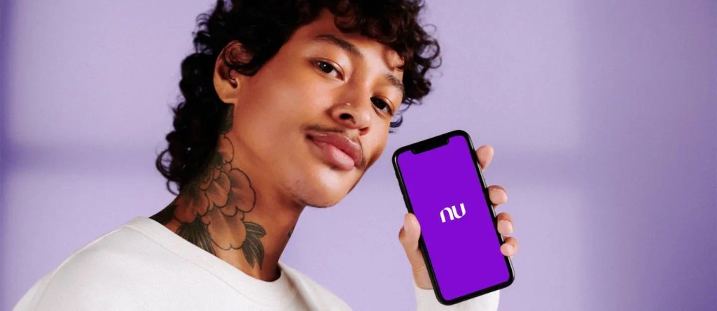 Tesouro Direto no Nubank: tudo o que você precisa saber. Um menino negro, de cabelos cacheados, segurando o celular como o logo do nubank no centro da tela em fundo roxo.